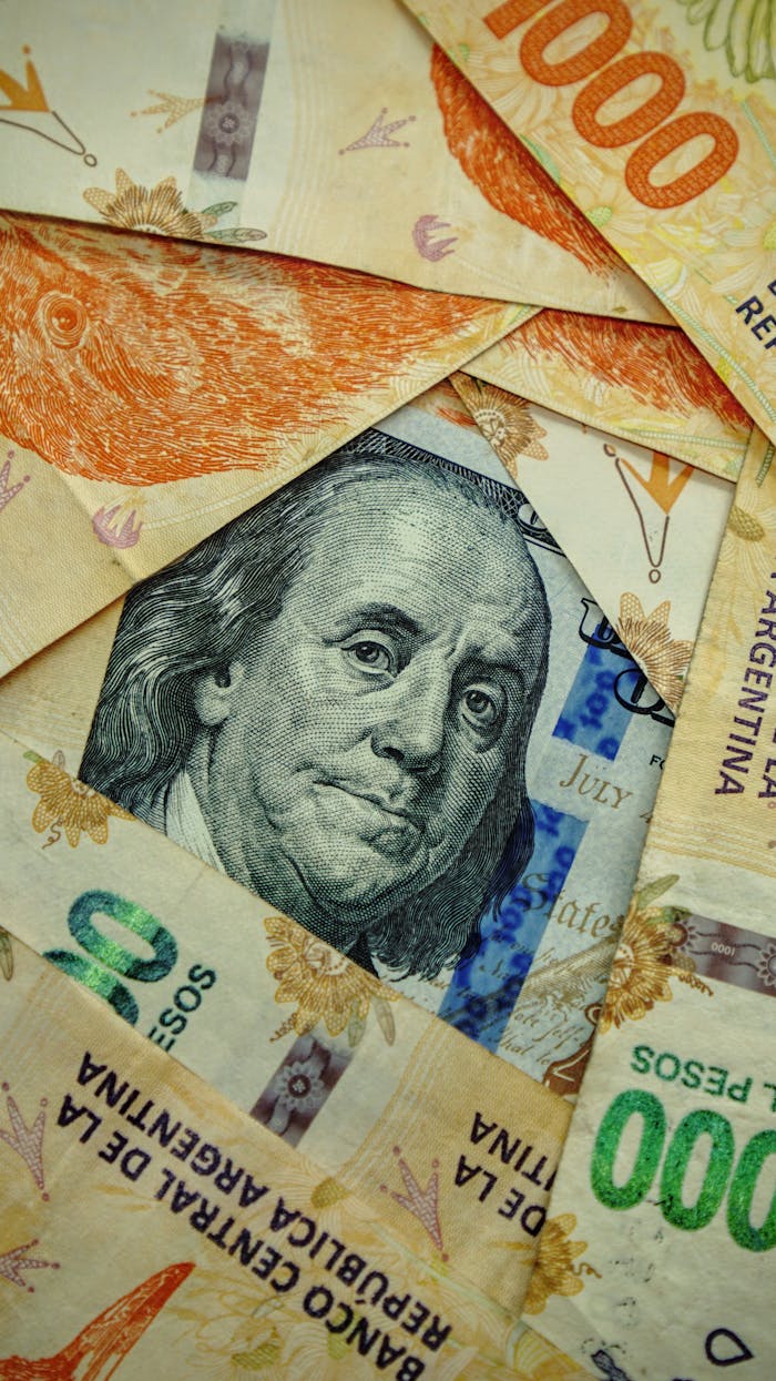 Close-up of US and Argentine banknotes featuring Benjamin Franklin and Argentine peso denominations.