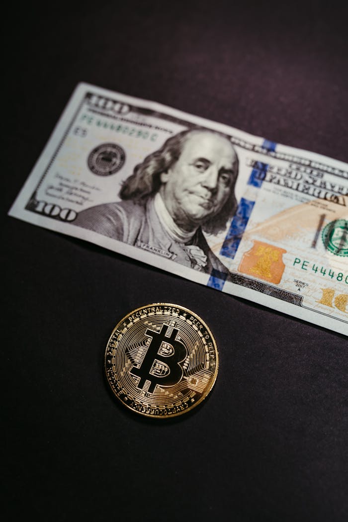 Close-up of a Bitcoin coin with a US 100 dollar bill, symbolizing digital and traditional currency.
